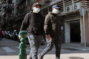 Two men walking in the street with protective masks on.
