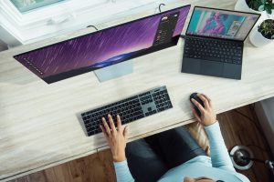 A view of a woman at a desk with two screens working from home.