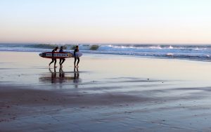 Three people with surfboards on a beach.